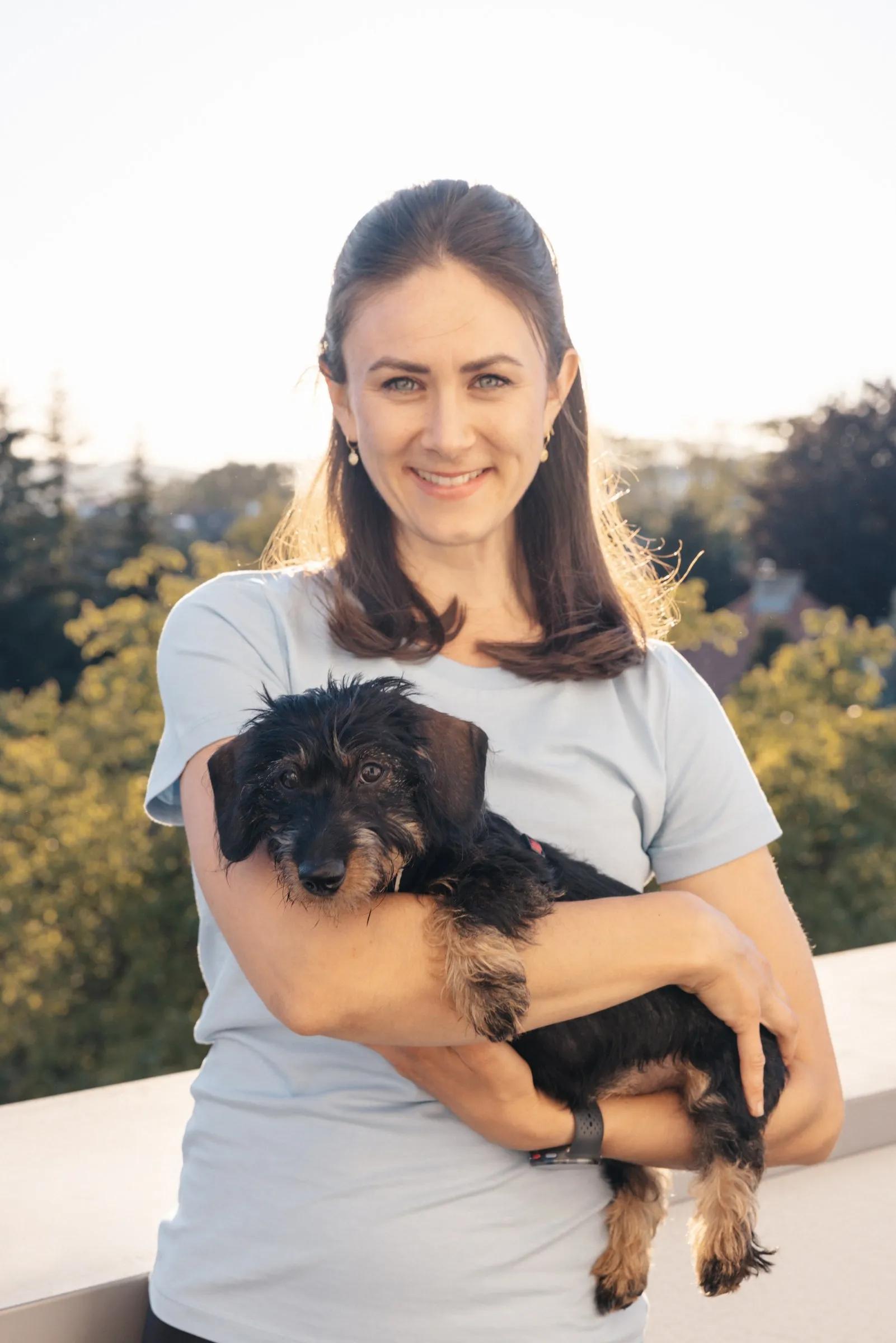 Johanna Penninger hält lachend einen kleinen Hund auf dem Arm, auf der Dachterrasse der Praxis