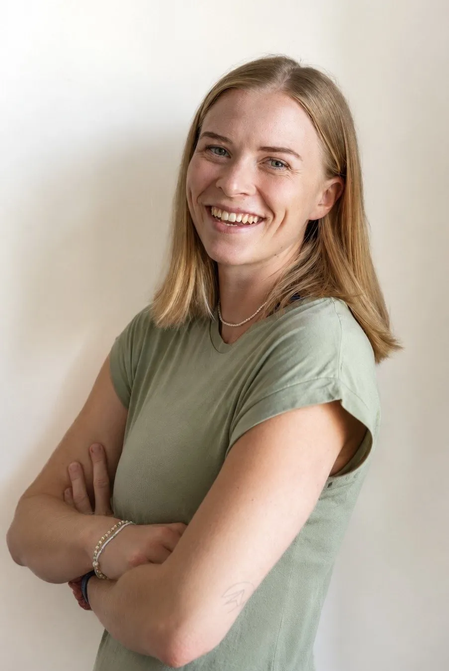 Stella Wittner steht mit verschränkten Armen lachend vor einer hellen Wand
