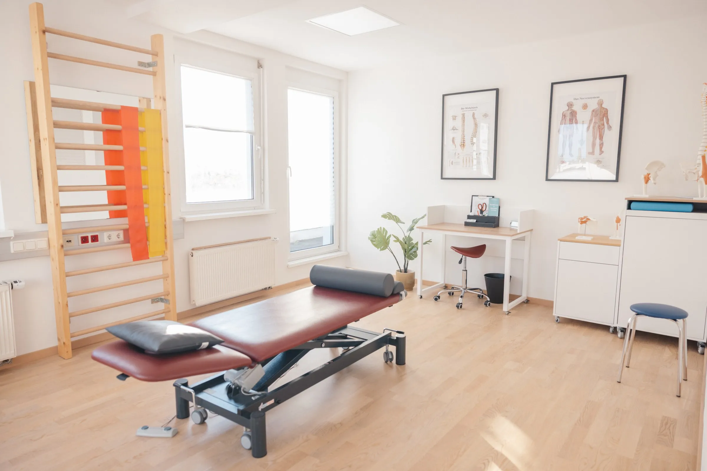 Heller Therapieraum mit Behandlungsliege, Sprossenwand und Anatomiepostern