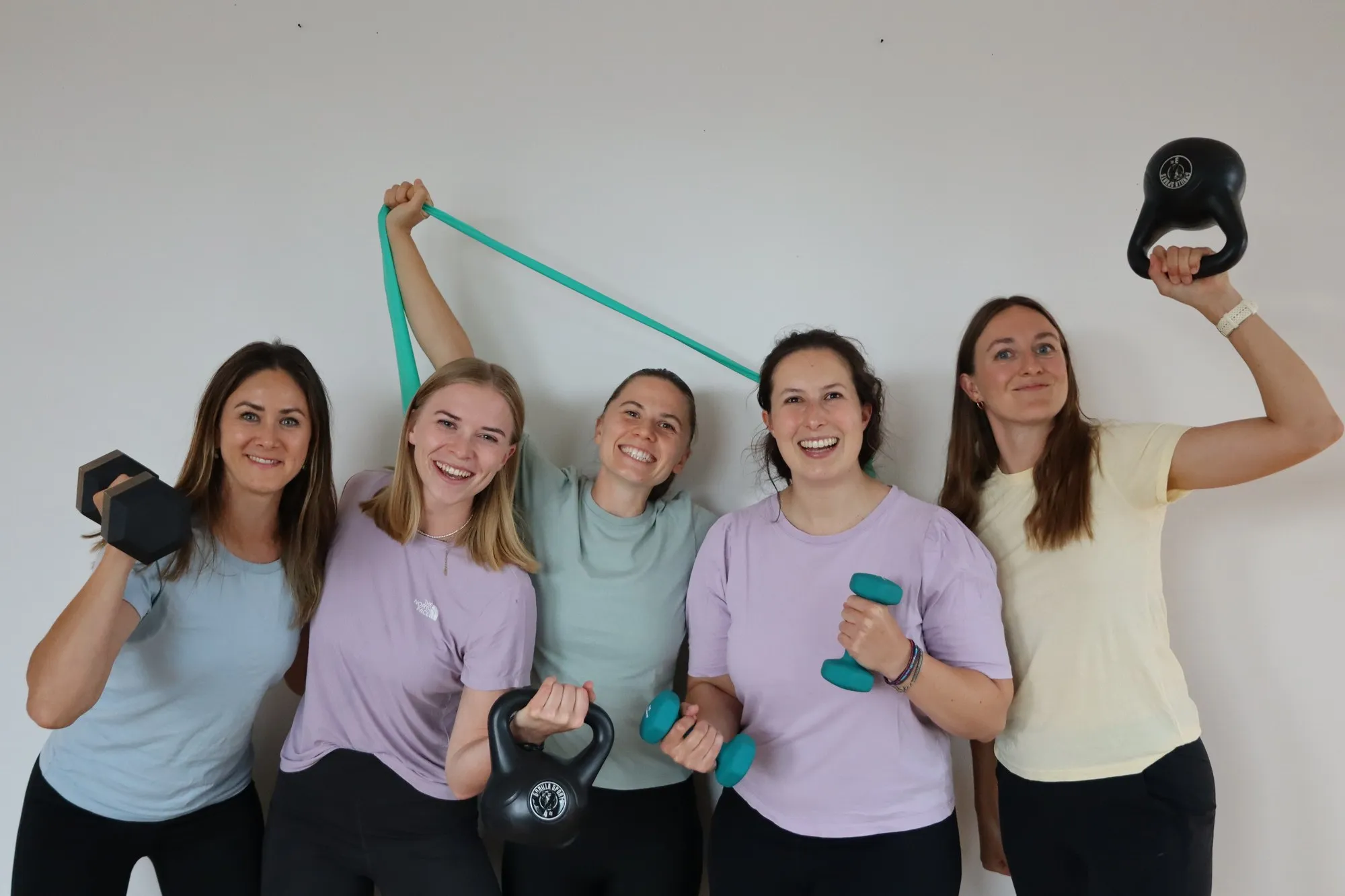 Das Team spannt ein Trainingsband und hält Gewichte hoch
